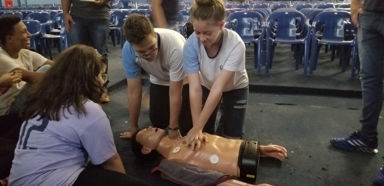 Imagem representando alunos aplicando técnica de reanimação cardiopulmonar em um boneco