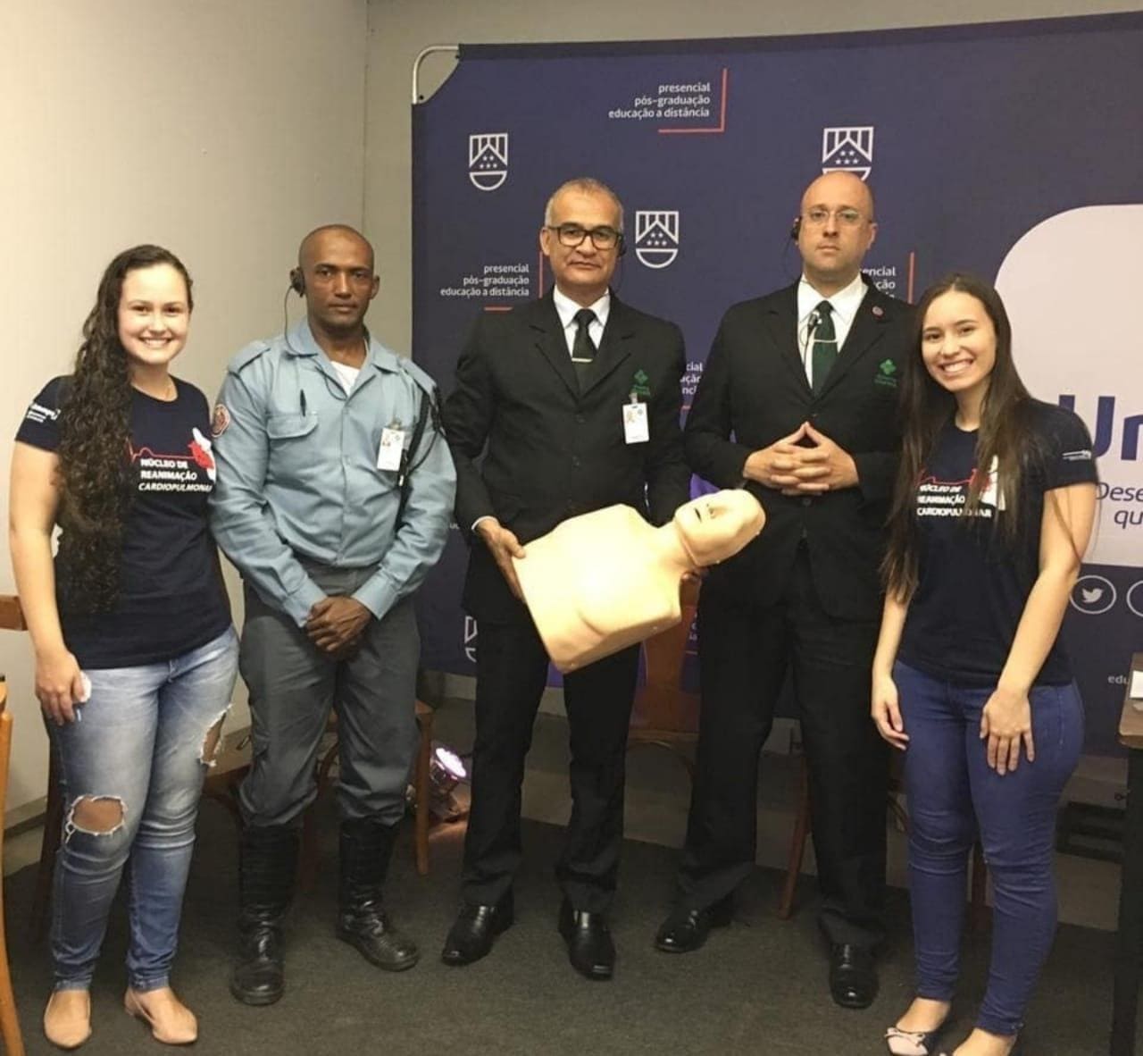 Imagem representando 5 pessoas e um boneco para testes de reanimação cardiopulmonar tirando foto