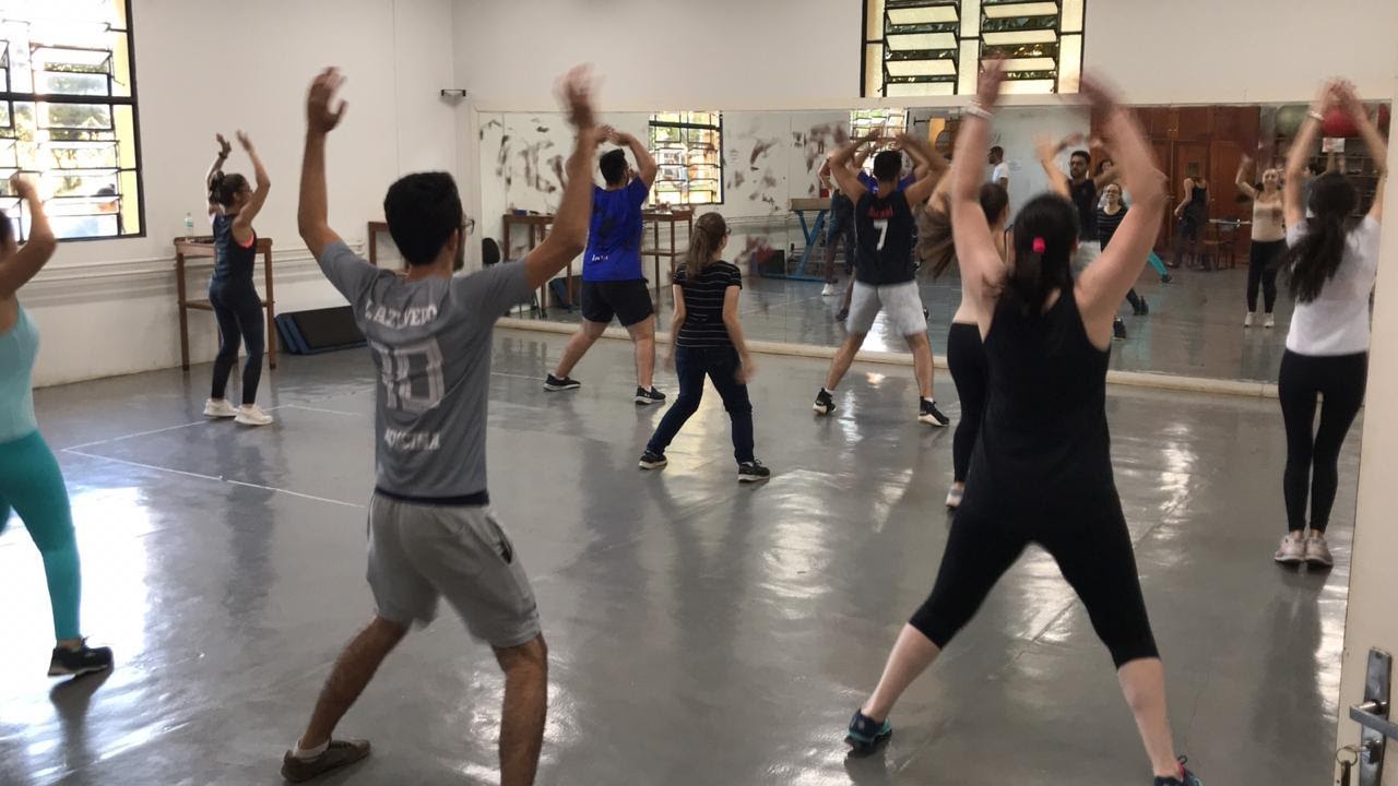 Imagem representando grupo de pessoas dançando em um studio com os braços para cima